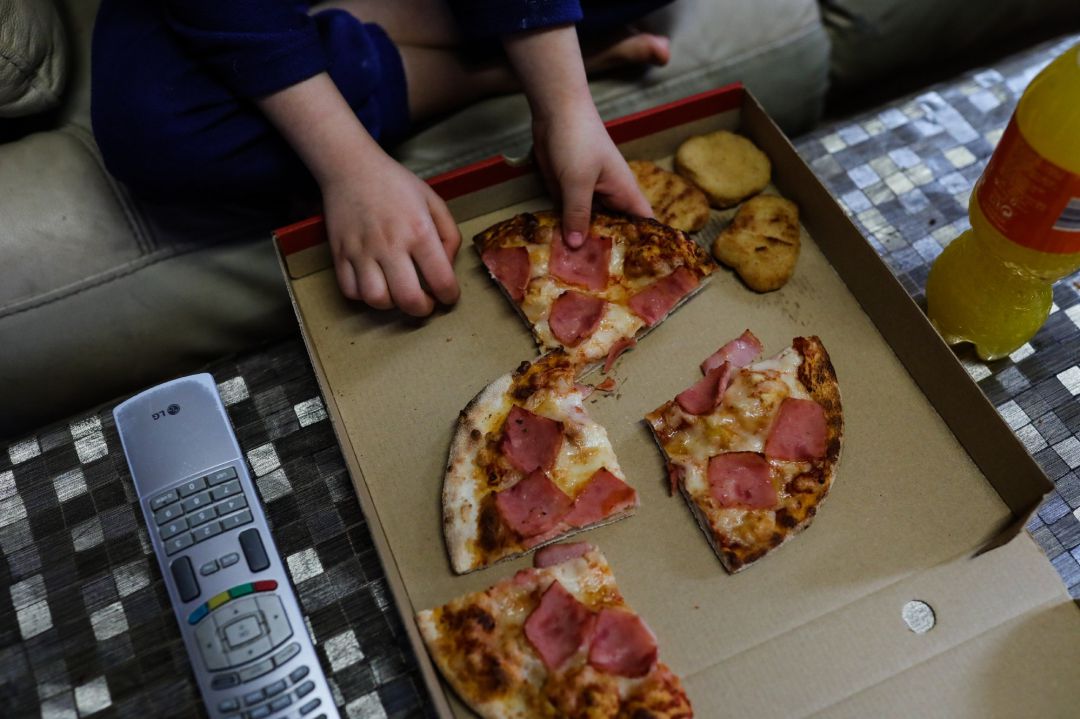 Un niño come pizza del menú infantil de Telepizza mientras ve la televisión en su casa Un niño come pizza del menú infantil de Telepizza mientras ve la televisión en su casa