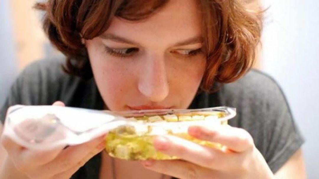 Una mujer huele un envase con comida Una mujer huele un envase con comida
