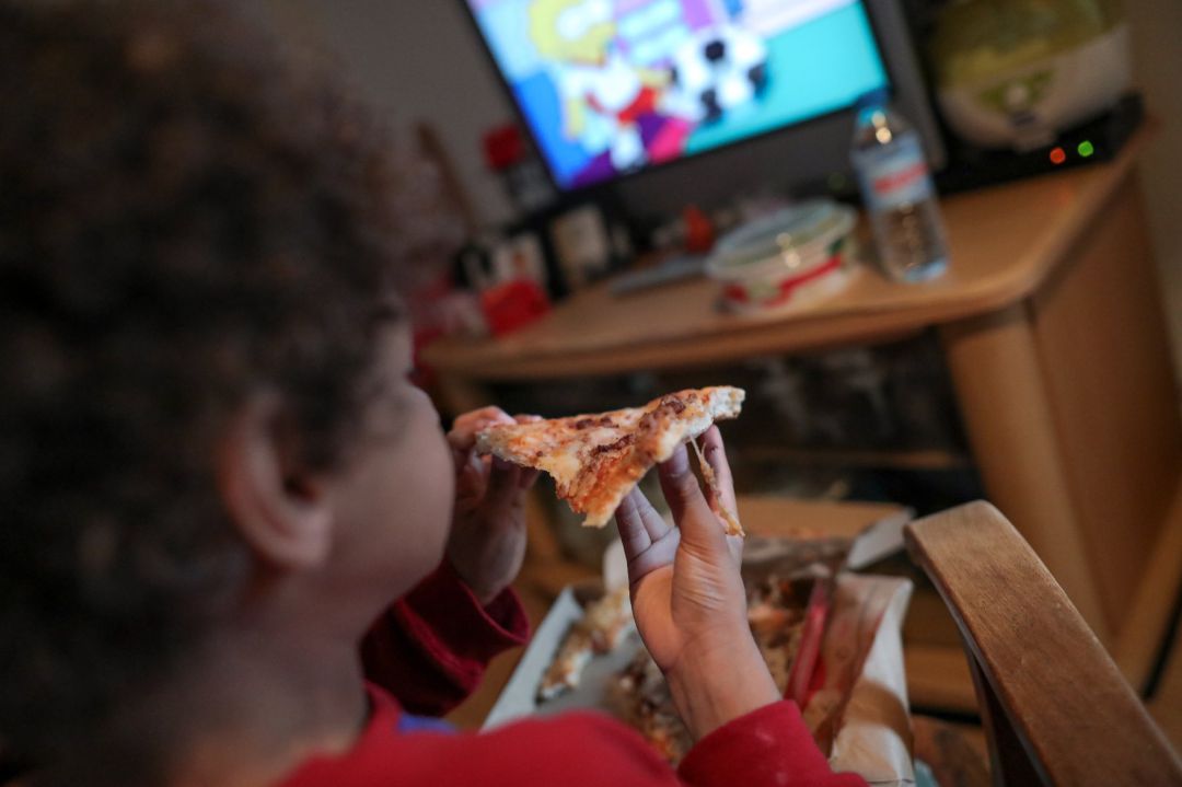 Un niño come un trozo de pizza del menú infantil de Telepizza mientras ve la televisión en su casa, tras recoger el menú en un establecimiento de Telepizza. Un niño come un trozo de pizza del menú infantil de Telepizza mientras ve la televisión en su casa, tras recoger el menú en un establecimiento de Telepizza.