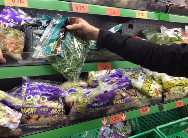 Una persona coge una bolsa de ensalada de un estante refrigerado en un supermercado.