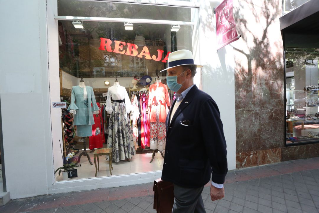 Un hombre protegido con mascarilla pasa junto a una tienda de ropa Un hombre protegido con mascarilla pasa junto a una tienda de ropa