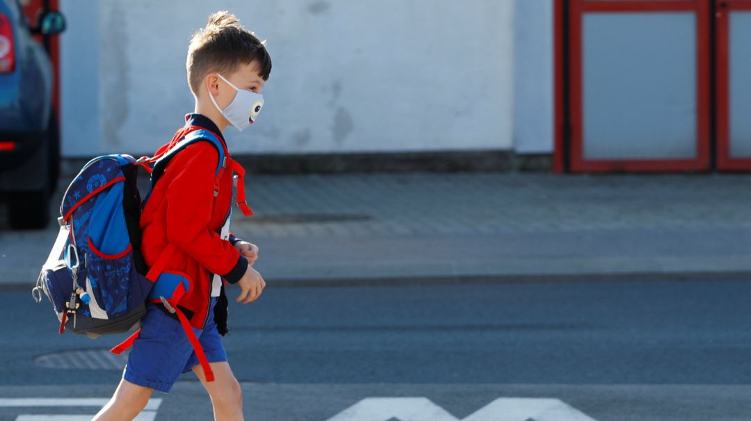 A child wearing a protective face mask walks a street as he arrives at a primary school A child wearing a protective face mask walks a street as he arrives at a primary school
