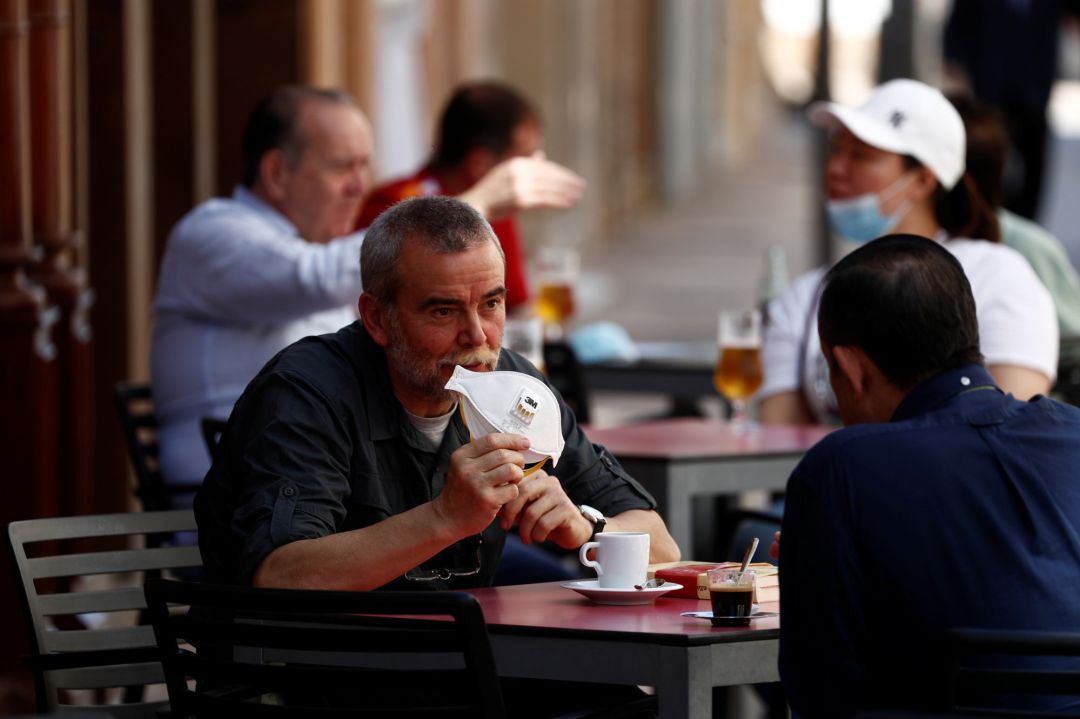 Varios ciudadanos tomando café, uno de ellos enseña su mascarilla de protección Varios ciudadanos tomando café, uno de ellos enseña su mascarilla de protección