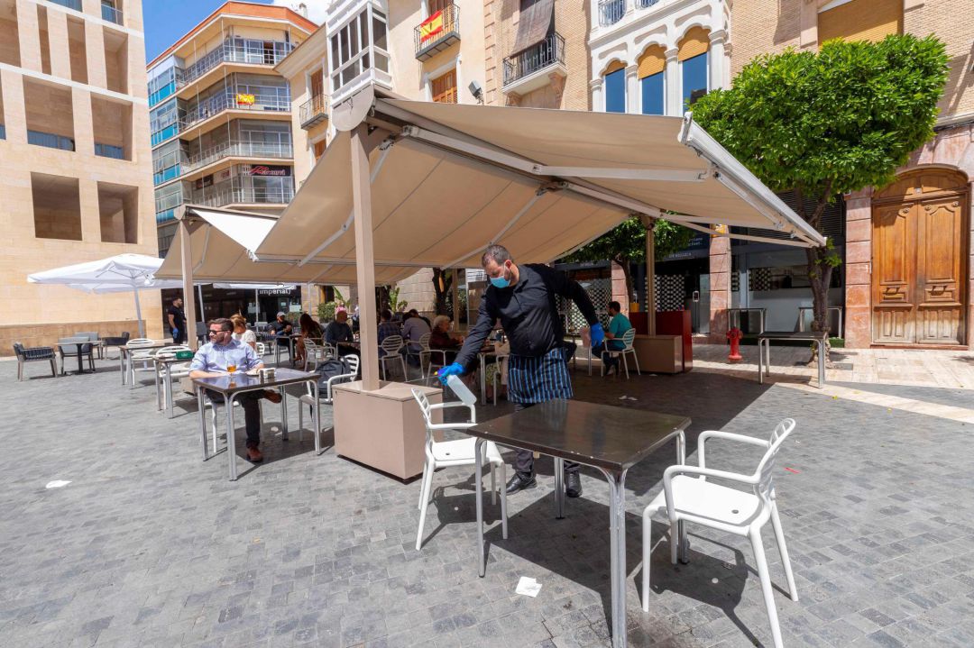 Un camarero desinfecta una mesa tras un servicio en una terraza de la Plaza de Belluga de Murcia, este lunes, primer dia de la fase 1 de desescalamiento por la pandemia del covid 19. Un camarero desinfecta una mesa tras un servicio en una terraza de la Plaza de Belluga de Murcia, este lunes, primer dia de la fase 1 de desescalamiento por la pandemia del covid 19.