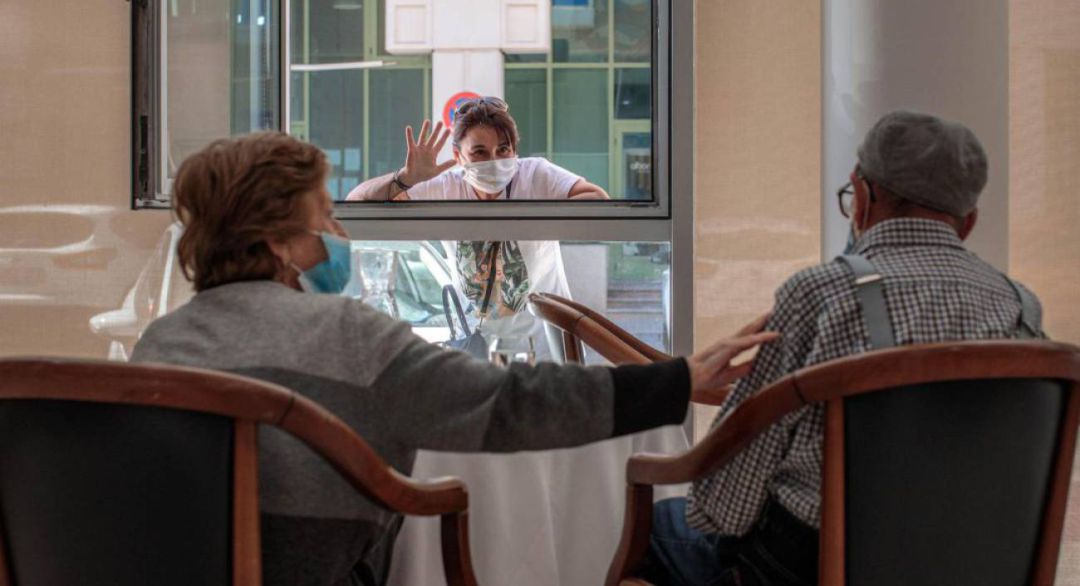 Una persona conversa con sus padres a través de una ventana habilitada en la residencia de mayores Una persona conversa con sus padres a través de una ventana habilitada en la residencia de mayores