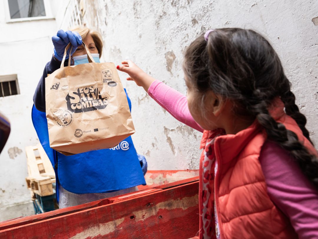 Imagen de una voluntaria de `Los salvacomidas´entregando un menú saludable a una niña Imagen de una voluntaria de `Los salvacomidas´entregando un menú saludable a una niña