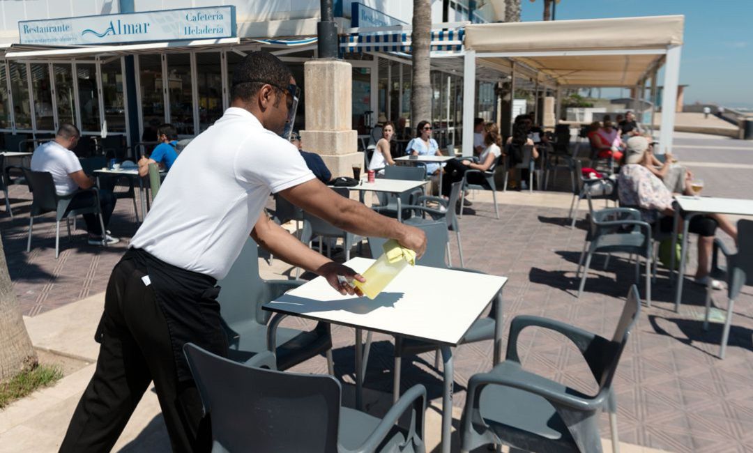 Un camarero desinfecta una mesa en un establecimiento hostelero Un camarero desinfecta una mesa en un establecimiento hostelero