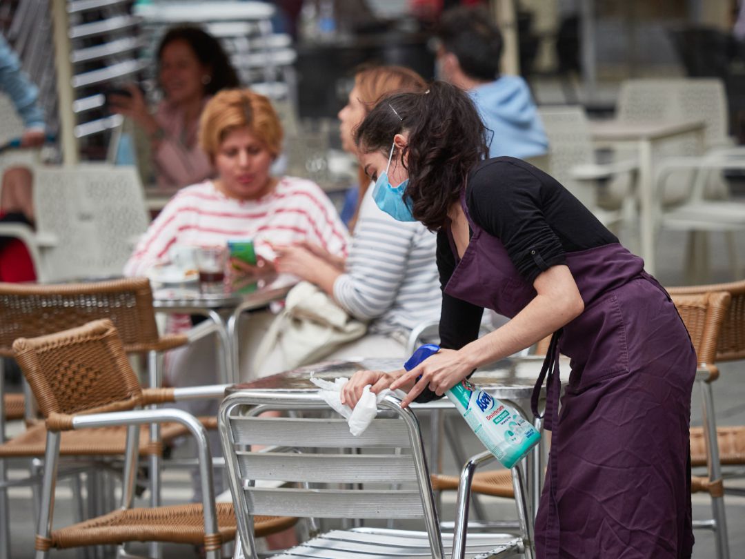 Una trabajadora desinfecta las mesas y sillas de una terraza Una trabajadora desinfecta las mesas y sillas de una terraza