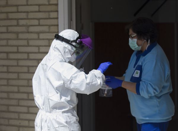 Un sanitario entrega las pruebas a otro, tras realizar una recogida de muestra desde el coche para detectar casos de coronavirus, (Covid-19), en el Hospital Militar de Sevilla.