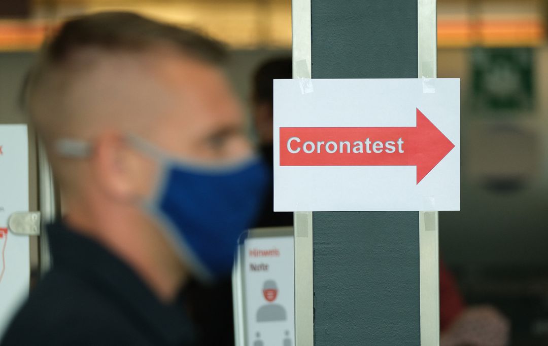 Un hombre con mascarilla junto a un cartel que indica que se realizan test de coronavirus. Un hombre con mascarilla junto a un cartel que indica que se realizan test de coronavirus.