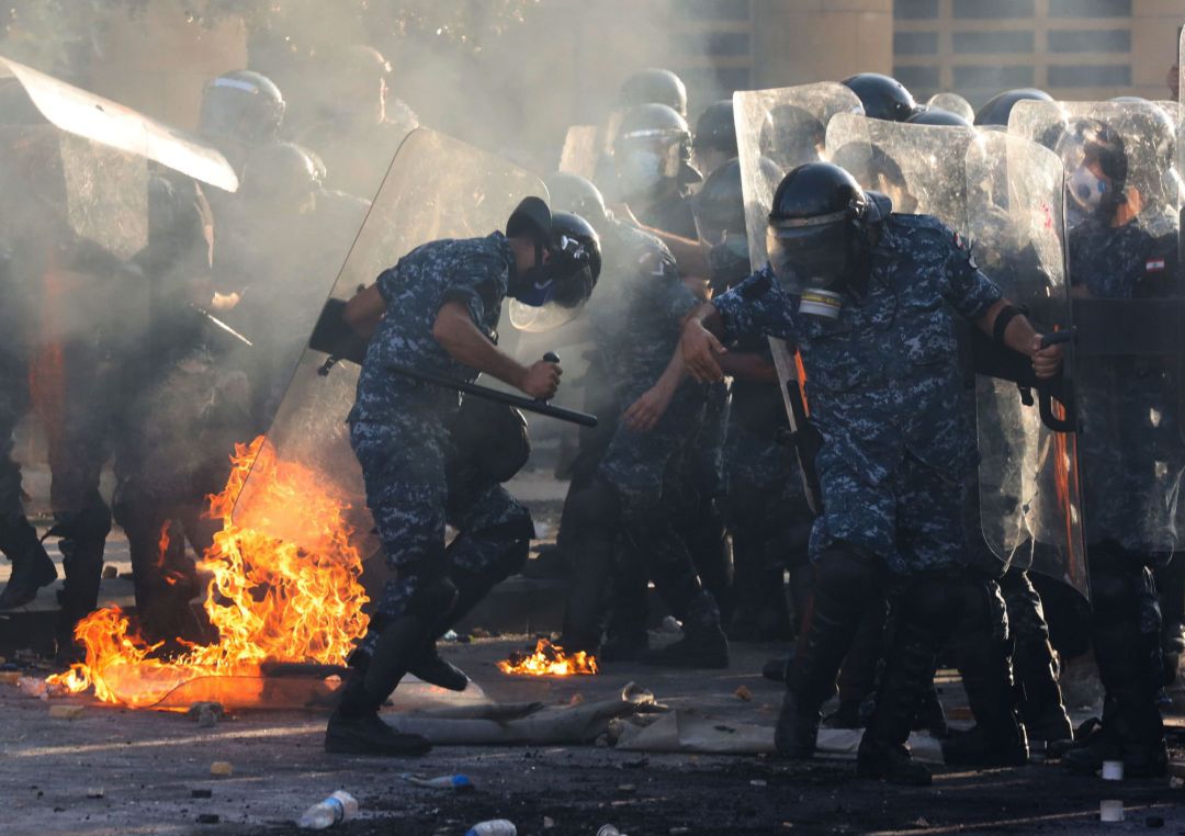 La policía antidisturbios libanesa intenta apagar un incendio cercano durante los enfrentamientos con manifestantes contra el gobierno en una protesta en Beirut, Líbano La policía antidisturbios libanesa intenta apagar un incendio cercano durante los enfrentamientos con manifestantes contra el gobierno en una protesta en Beirut, Líbano