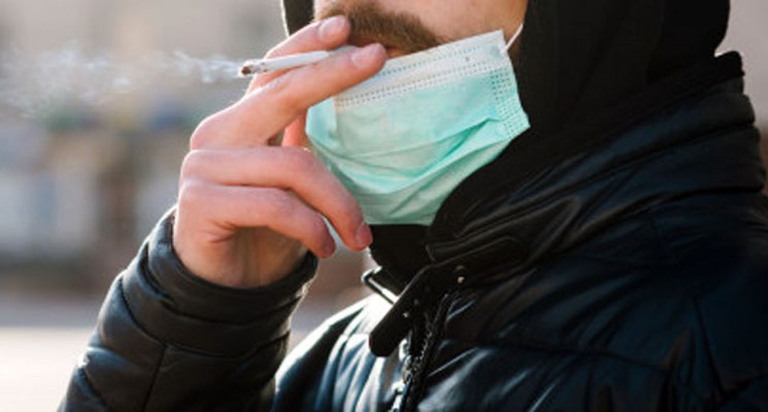 Un hombre con mascarilla fuma un cigarro. Un hombre con mascarilla fuma un cigarro.