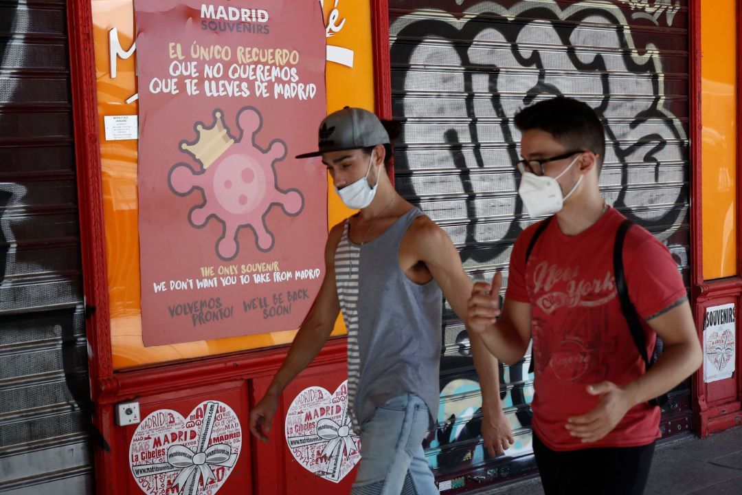 Dos jóvenes pasan ante un cartel alusivo al coronavirus en el centro de Madrid Dos jóvenes pasan ante un cartel alusivo al coronavirus en el centro de Madrid