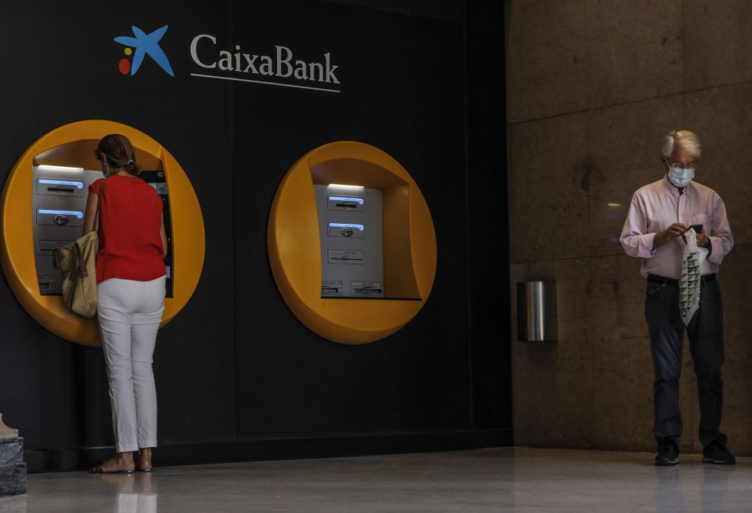 Dos personas en los cajeros dispuestos en el edificio de la sede de Caixabank, en Valencia Dos personas en los cajeros dispuestos en el edificio de la sede de Caixabank, en Valencia