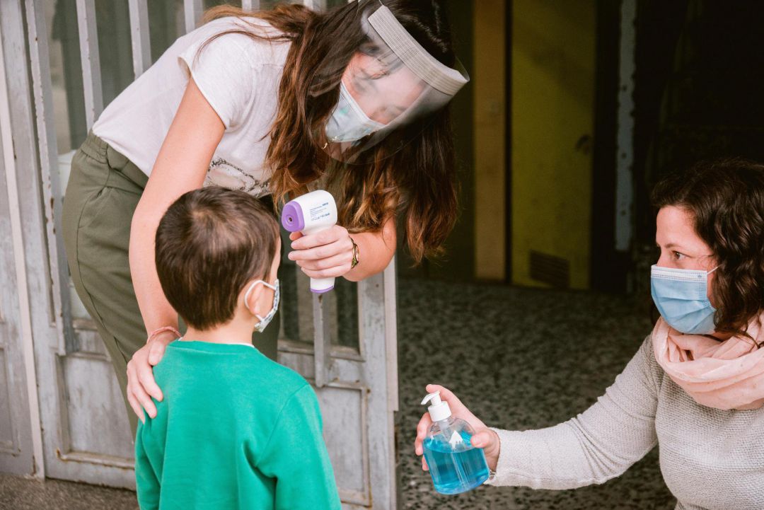 Dos trabajadoras de un centro educativo toman la temperatura y aplican gel hidroalcohólico en las manos a un niño. Dos trabajadoras de un centro educativo toman la temperatura y aplican gel hidroalcohólico en las manos a un niño.