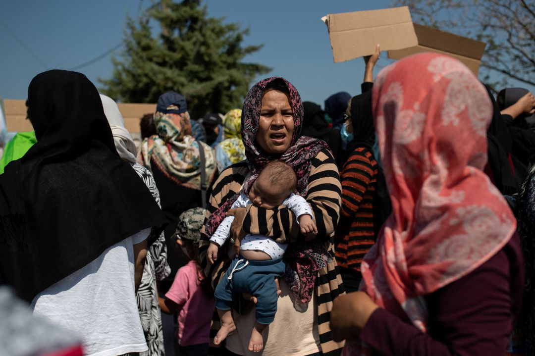 A woman holds a baby as refugees and migrants from the destroyed Moria camp protest near a new temporary camp, on the island of Lesbos, Greece, September 14, 2020 A woman holds a baby as refugees and migrants from the destroyed Moria camp protest near a new temporary camp, on the island of Lesbos, Greece, September 14, 2020