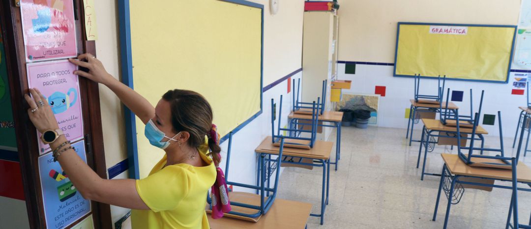 Una profesora coloca carteles de medidas preventivas ante el COVID-19 en el aula antes del inicio del curso escolar en un colegio. Una profesora coloca carteles de medidas preventivas ante el COVID-19 en el aula antes del inicio del curso escolar en un colegio.