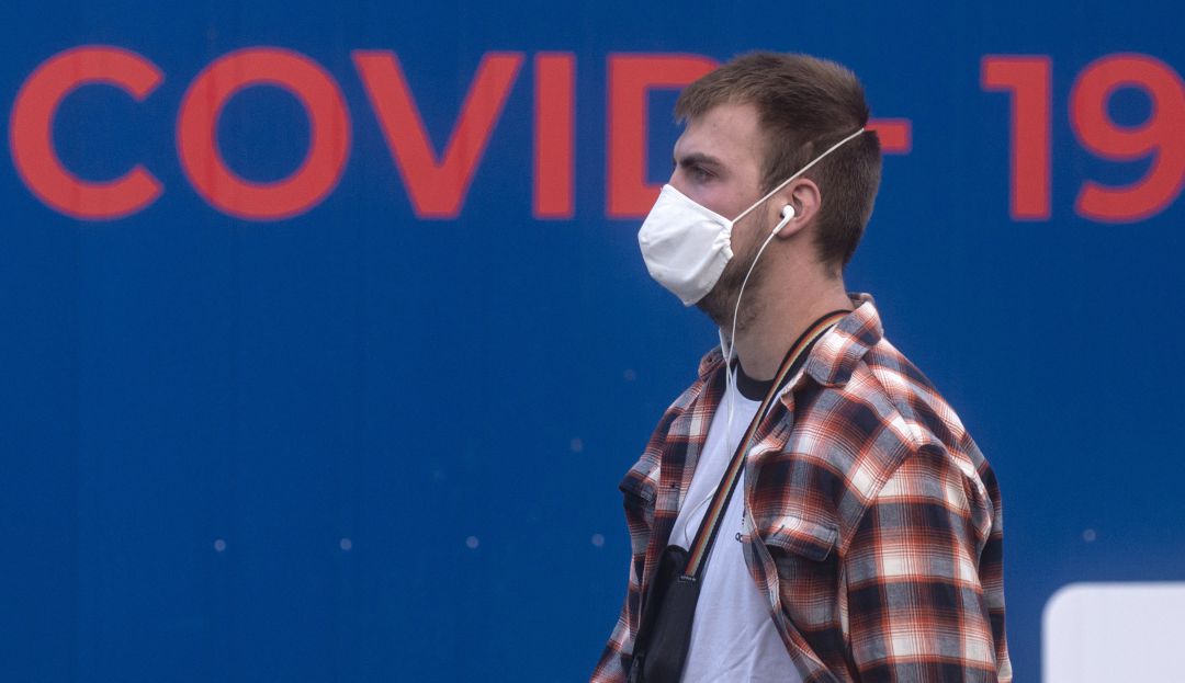 Un joven camina con una mascarilla puesta. Un joven camina con una mascarilla puesta.