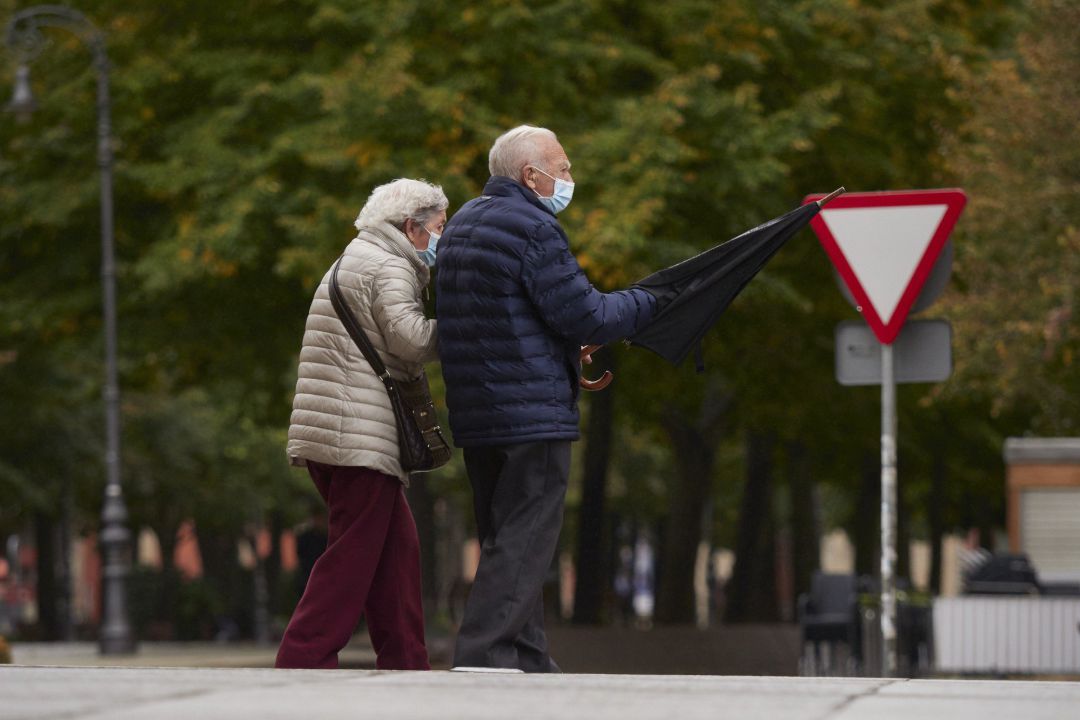 Una pareja de personas mayores, protegidas con mascarillas, pasea por la calle de una ciudad. Una pareja de personas mayores, protegidas con mascarillas, pasea por la calle de una ciudad.