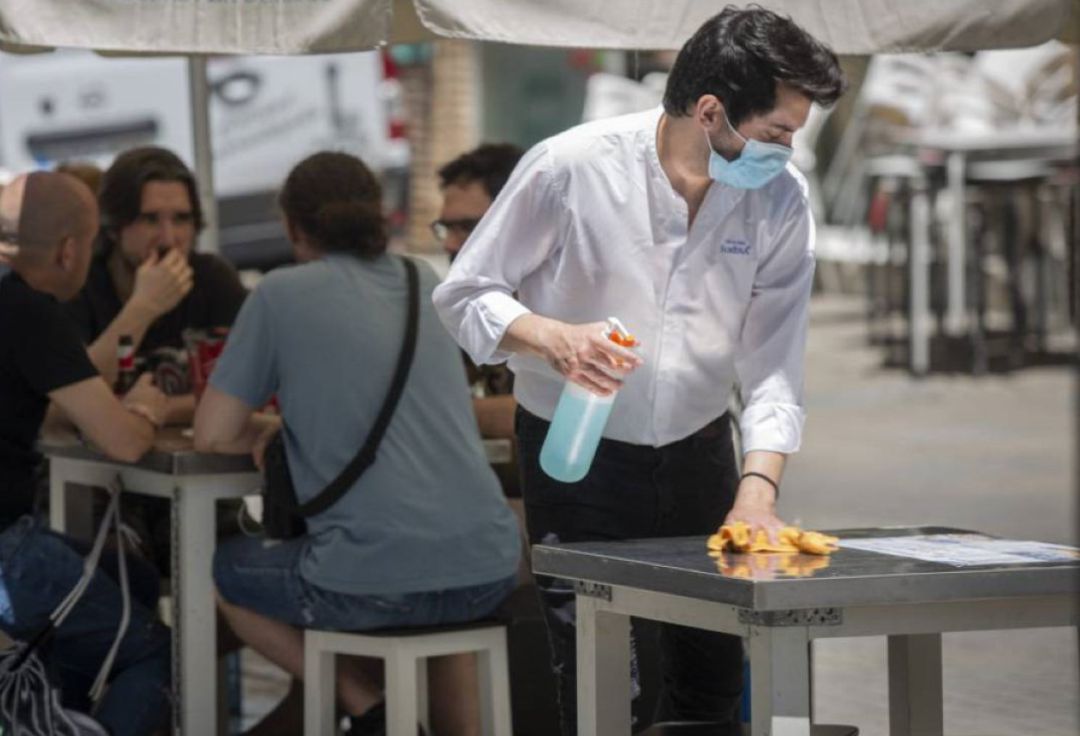 Un camarero desinfecta lamesa de la terraza del establecimiento Un camarero desinfecta lamesa de la terraza del establecimiento