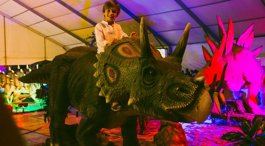 Un menor disfruta subido a un dinosaurio. Un menor disfruta subido a un dinosaurio.