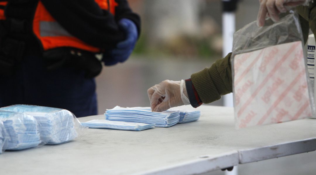 Transeúntes recogen mascarillas puestas a disposición de viajeros y usuarios de transporte público en las inmediaciones de una estación. Transeúntes recogen mascarillas puestas a disposición de viajeros y usuarios de transporte público en las inmediaciones de una estación.