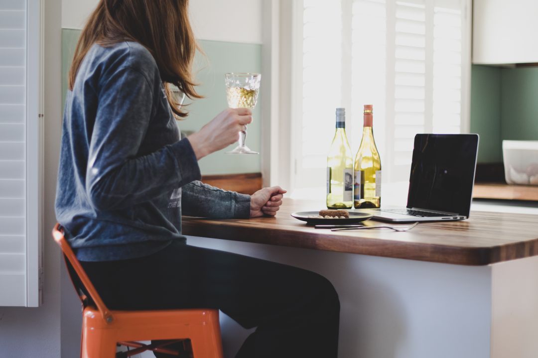 Una mujer sujeta una copa de vino junto a dos botellas de la misma bebida en un domicilio, frente a un ordenador. Una mujer sujeta una copa de vino junto a dos botellas de la misma bebida en un domicilio, frente a un ordenador.