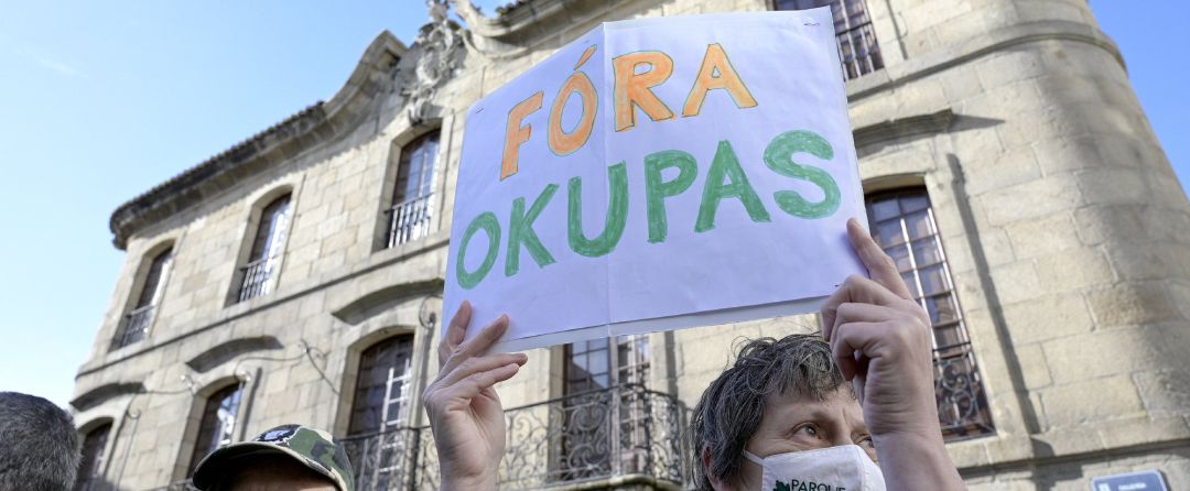 Una persona sostiene un cartel donde se puede leer "Fuera okupas" durante una marcha cívica para pedir la devolución de la Casa Cornide Una persona sostiene un cartel donde se puede leer "Fuera okupas" durante una marcha cívica para pedir la devolución de la Casa Cornide