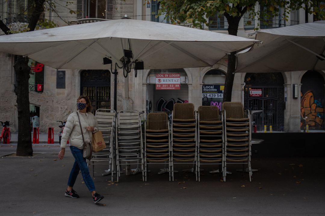 Una mujer pasa junto a la terraza recogida de un bar cerrado. Una mujer pasa junto a la terraza recogida de un bar cerrado.