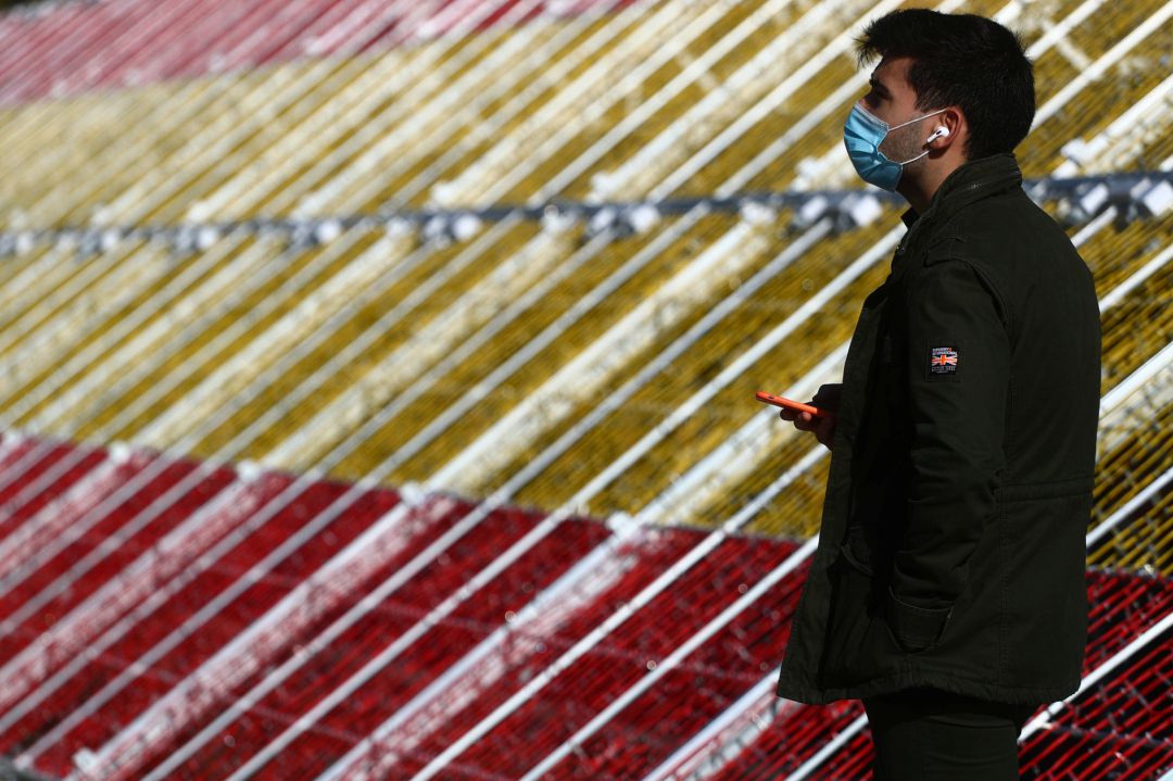 Un hombre con mascarilla pasa delante de la bandera de España con luces instalada en Madrid. Un hombre con mascarilla pasa delante de la bandera de España con luces instalada en Madrid.