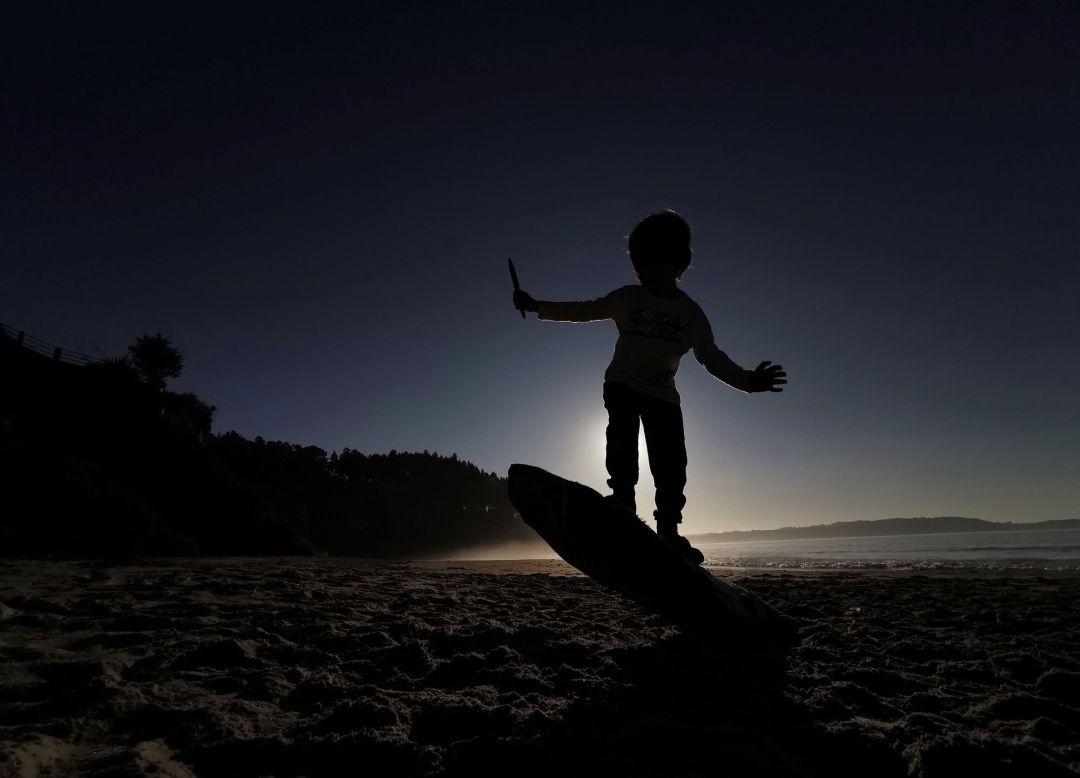Un niño hace equilibrios sobre el tronco de un árbol arrastrado por el mar a una playa, en una imagen de archivo Un niño hace equilibrios sobre el tronco de un árbol arrastrado por el mar a una playa, en una imagen de archivo
