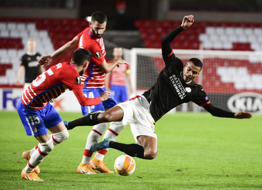 El delantero del PSV, Donyell Malen (d), cae ante los jugadores del Granada, Carlos Neva (i) y el francés, Maxime Gonalons, durante el encuentro correspondiente a la fase de grupos de la Liga Europa que han disputado este jueves en el estadio Nuevo Los Cármenes, en Granada. El delantero del PSV, Donyell Malen (d), cae ante los jugadores del Granada, Carlos Neva (i) y el francés, Maxime Gonalons, durante el encuentro correspondiente a la fase de grupos de la Liga Europa que han disputado este jueves en el estadio Nuevo Los Cármenes, en Granada.
