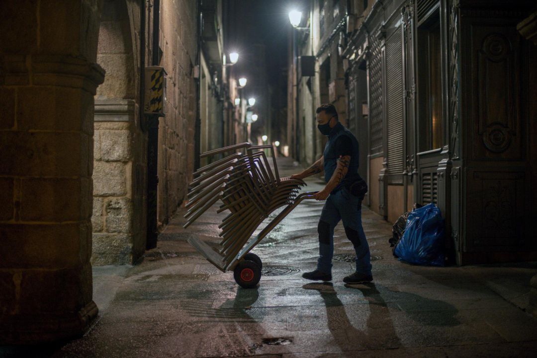 Un empleado recoge las sillas de la terraza en la plaza mayor Un empleado recoge las sillas de la terraza en la plaza mayor