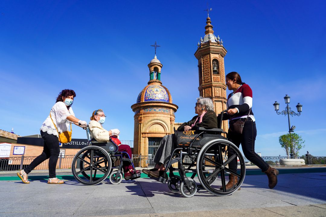 Dos personas mayores en silla de ruedas se saludan a la entrada del Puente de Triana, en Sevilla (Andalucía). Dos personas mayores en silla de ruedas se saludan a la entrada del Puente de Triana, en Sevilla (Andalucía).
