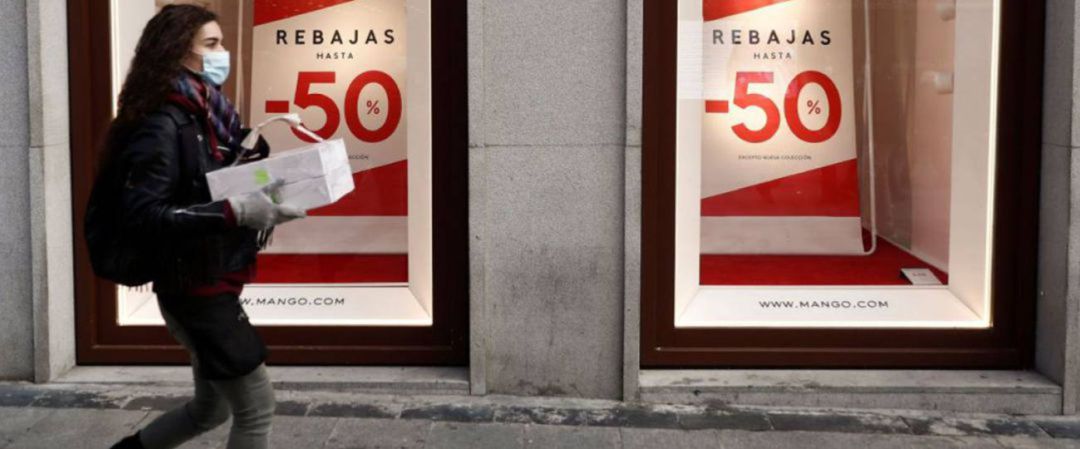 Una mujer pasea con un paquete delante de un escaparate en Rebajas. Una mujer pasea con un paquete delante de un escaparate en Rebajas.