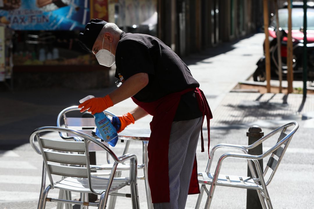 Un camarero limpia las mesas y sillas de una terraza de un bar Un camarero limpia las mesas y sillas de una terraza de un bar