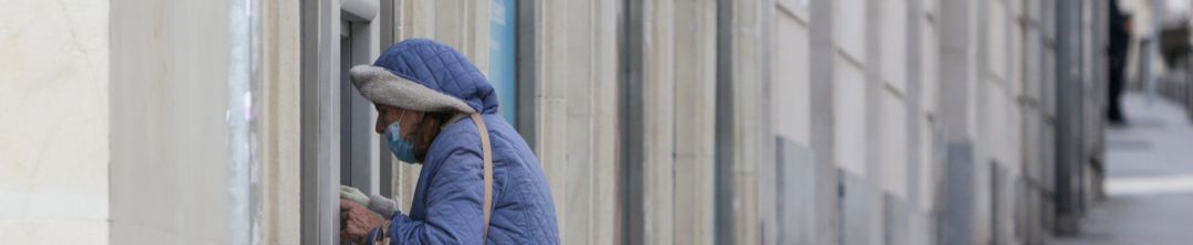 Una mujer protegida con mascarilla y abrigada saca dinero de un cajero Una mujer protegida con mascarilla y abrigada saca dinero de un cajero