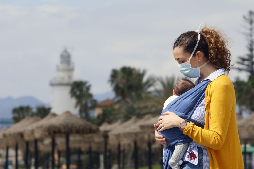 Una mujer protegida con una mascarilla da un paseo con su bebé. Una mujer protegida con una mascarilla da un paseo con su bebé.