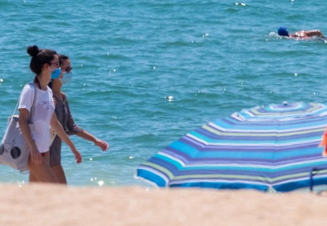 Dos mujeres pasean por la playa llevando mascarilla Dos mujeres pasean por la playa llevando mascarilla
