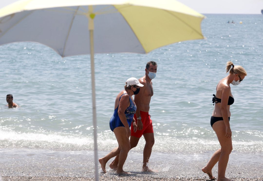 Bañistas con mascarilla pasean por la orilla de una playa. Bañistas con mascarilla pasean por la orilla de una playa.