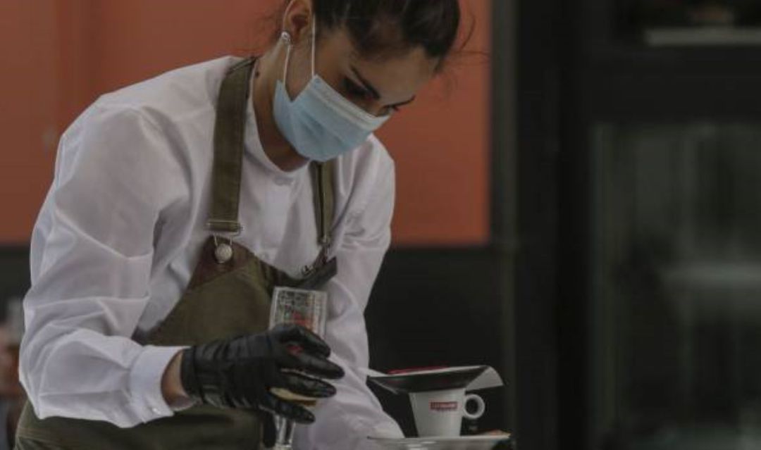 Una camarera con mascarilla y guantes atiende un bar Una camarera con mascarilla y guantes atiende un bar