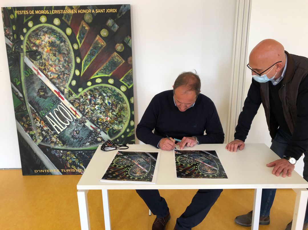 El pintor Luis Sanus firmando una de las postales de su cartel ante el director del Economato, Juanjo Garrido, con el cartel al fondo El pintor Luis Sanus firmando una de las postales de su cartel ante el director del Economato, Juanjo Garrido, con el cartel al fondo