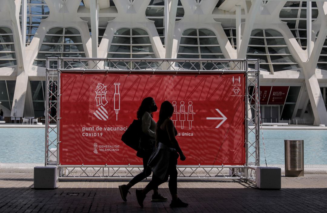 Dos personas pasan por un cartel que indica el punto de vacunación de la Ciudad de las Artes y las Ciencias de València de cara al inicio de la vacunación masiva contra la covid-19. Dos personas pasan por un cartel que indica el punto de vacunación de la Ciudad de las Artes y las Ciencias de València de cara al inicio de la vacunación masiva contra la covid-19.