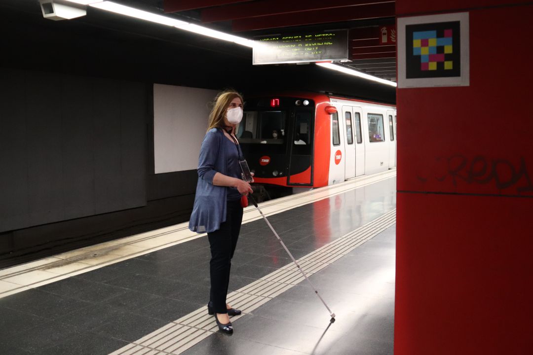Una dona amb discapacitat visual esperant el metro al costat d'una etiqueta intel·ligent a l'estació de metro de Plaça Universitat Una dona amb discapacitat visual esperant el metro al costat d'una etiqueta intel·ligent a l'estació de metro de Plaça Universitat