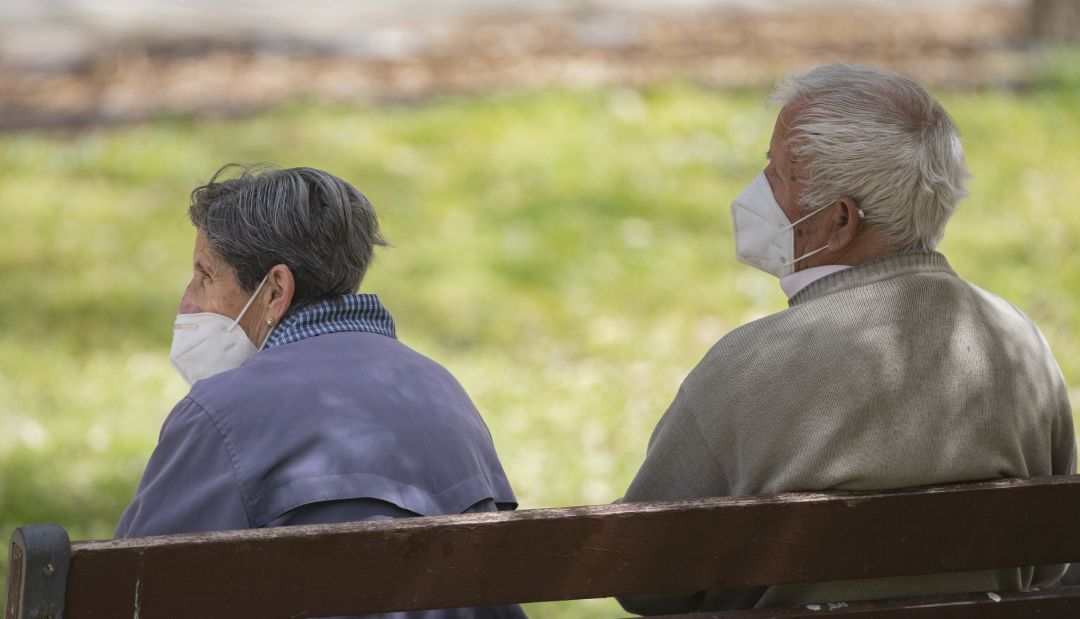 Un hombre y una mujer mayores, sentados en un banco y con mascarilla Un hombre y una mujer mayores, sentados en un banco y con mascarilla