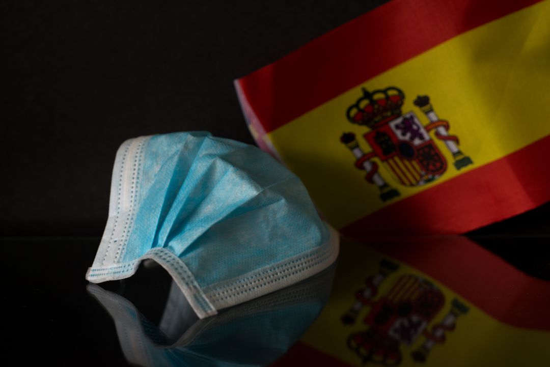 Imagen de archivo de una mascarilla quirúrgica y una bandera de España. Imagen de archivo de una mascarilla quirúrgica y una bandera de España.