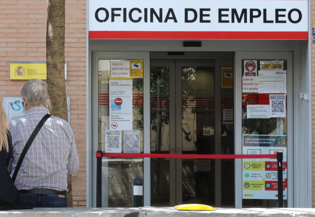 Dos personas sentadas frente a una oficina del SEPE Dos personas sentadas frente a una oficina del SEPE