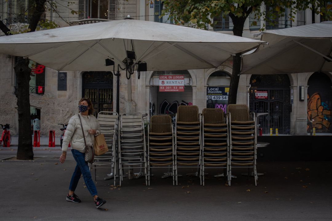 Una mujer pasa junto a la terraza recogida de un bar cerrado. Una mujer pasa junto a la terraza recogida de un bar cerrado.