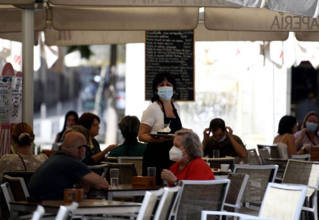 Una camarera con mascarilla atiende a los clientes en una terraza de un ba Una camarera con mascarilla atiende a los clientes en una terraza de un ba