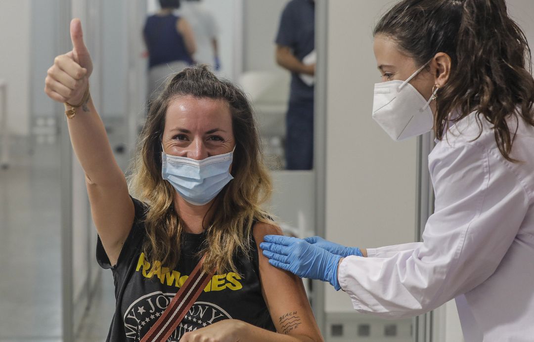 Una joven sonríe y saluda mientras recibe la vacuna contra la COVID-19. Una joven sonríe y saluda mientras recibe la vacuna contra la COVID-19.